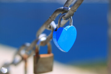 Blue heart shaped padlock as symbol of eternal love hanging on chain with sea view. Old rusty love locks on chain. Vintage colorful padlocks heart shaped on blue background. Couple. Clip art. Cards