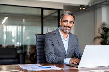 Portrait of mature Indian or Latin business man ceo trader using laptop computer, typing, working...