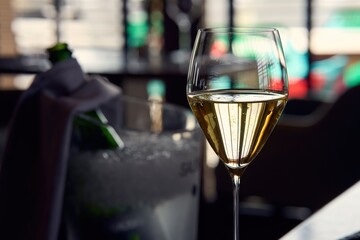Glass of champagne on table in elegant, fancy restaurant. Champagne bottle and bucket in background.