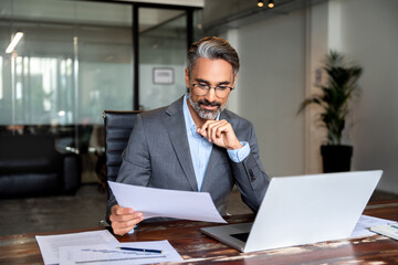 Busy Latin or Indian male business man accountant analyst holding documents, work at laptop...