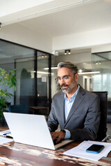 Vertical portrait of middle-age Hispanic man using laptop for business studying, watch online virtual webinar training, video call meeting. Focused mature Indian or Latin businessman work in office.