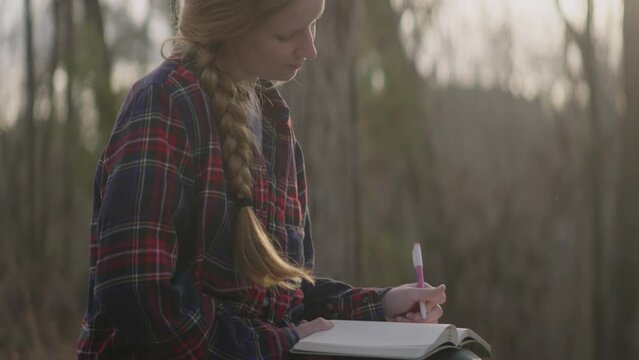 Smiling young woman reading her bible, writing notes, and admiring nature