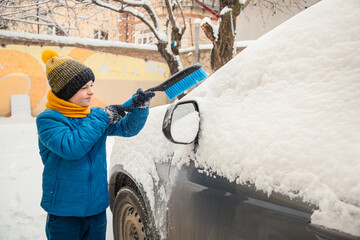 Cute little boy is helping his father brush the snow from the car. Snow removal from the car...
