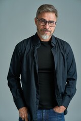 Fototapeta premium Portrait of happy casual older bearded man with glasses and gray hair smiling, Mid adult, mature age guy standing, isolated on gray background.
