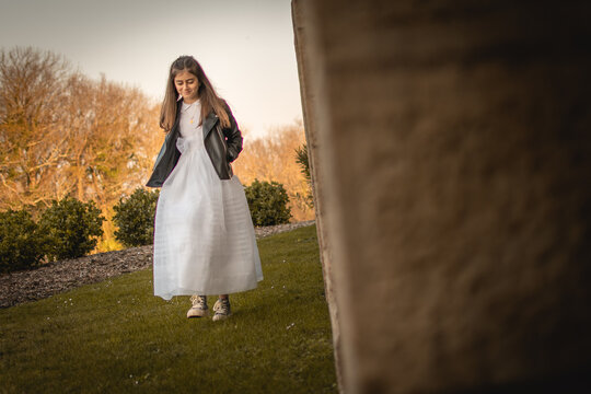Girl celebrating her first communion with a white communion dress and black leather jacket, walking in the gardens of a castle