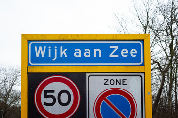 Place name sign of the coastal village of Wijk aan Zee, The Netherlands. Below are signs of a speed limit of 50 and a no parking sign.