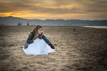 Girl with first communion dress and leather jacket celebrating her day on the beach during a sunset
