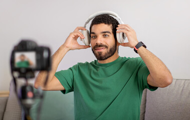 Content creator in a casual green t-shirt enjoys music on white headphones, smiling at the camera - obrazy, fototapety, plakaty