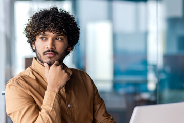 Pensive young businessman with curly hair looks away thoughtfully, portraying determination and...