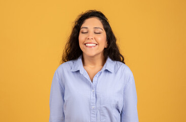 Fototapeta premium Radiant young woman with closed eyes and a joyful smile, wearing a light blue shirt