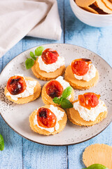 Crostini on crispbread with ricotta, baked tomatoes and basil on a plate vertical view
