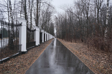 road goes into the distance in autumn during the rain along a white fence