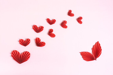 Composition of folded red paper hearts and leaves on a pink background top view