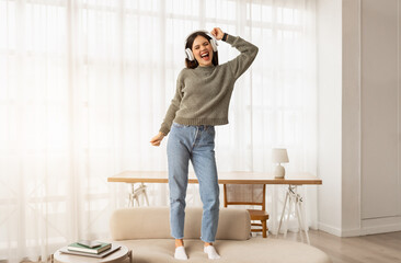 Carefree young woman dancing on couch, listening to music