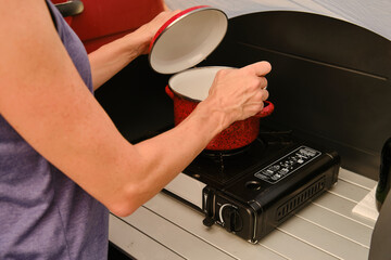 Crop woman preparing food on electric stove during trip