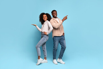 Happy black couple pointing sideways at free space on blue background