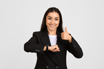 Smiling businesswoman giving thumbs up and checking watch