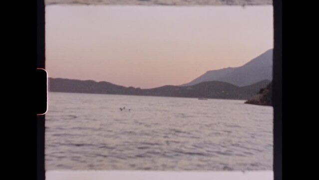 Man dives off a cliff and head-first into the ocean at sunset. Shot on 8mm