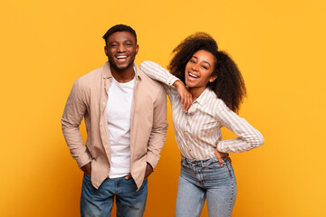 Cheerful young black couple laughing together against yellow background - obrazy, fototapety, plakaty