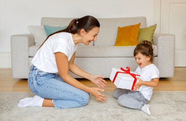 Excited little daughter receiving gift from mom at home