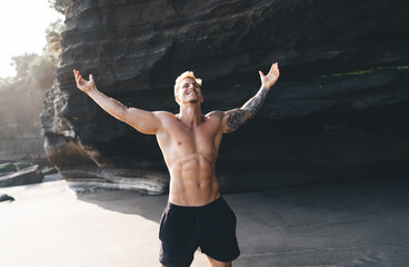 Fototapeta premium Shirtless excited man with raised arms on sandy beach