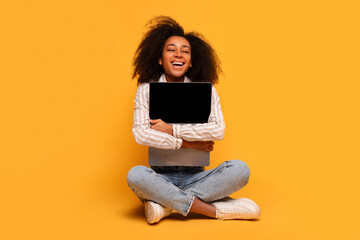 Happy young black woman holding laptop on yellow background