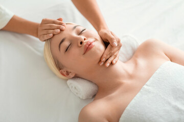 Fototapeta na wymiar blonde woman enjoying facial massage lying on spa bed indoor