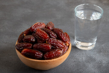 Glass of water with a bowl of date fruit on black background
