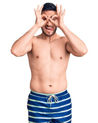 Fototapeta premium Young handsome man wearing swimwear doing ok gesture like binoculars sticking tongue out, eyes looking through fingers. crazy expression.