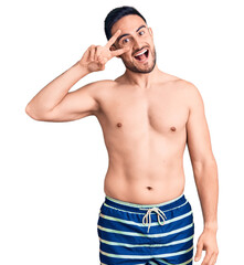 Fototapeta premium Young handsome man wearing swimwear doing peace symbol with fingers over face, smiling cheerful showing victory
