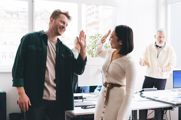 Joyful male and female creative coworkers rejoicing with new startup idea making high five gesture...