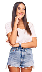 Fototapeta premium Young hispanic woman wearing casual white tshirt with hand on chin thinking about question, pensive expression. smiling and thoughtful face. doubt concept.