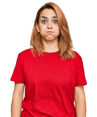 Hispanic young woman wearing casual red t shirt puffing cheeks with funny face. mouth inflated with...