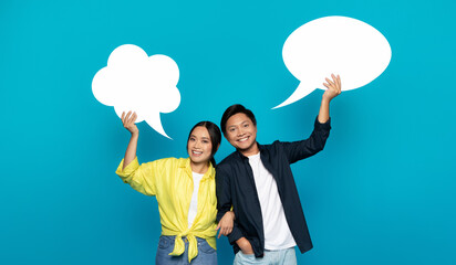 An exuberant Asian couple joyfully holds up speech bubbles, symbolizing lively conversation