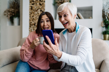 Amazed aged multiracial female friends using cellphone at home