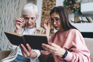 Senior multiracial girlfriends adjusting glasses while watching photo album
