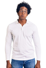 Handsome african american man with afro hair wearing casual clothes and glasses puffing cheeks with...