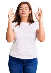 Middle age latin woman wearing casual white tshirt relaxed and smiling with eyes closed doing meditation gesture with fingers. yoga concept.