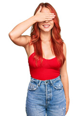 Young redhead woman wearing casual clothes smiling and laughing with hand on face covering eyes for surprise. blind concept.