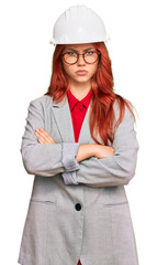 Young redhead woman wearing architect hardhat skeptic and nervous, disapproving expression on face with crossed arms. negative person.