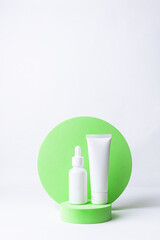 Minimalism style composition with white unbranded cosmetic tube and bottle with dropper on bright green cosmetic podium on white background. Cosmetic sale and promo banner, copy space for your design.