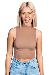 Beautiful young blonde woman wearing casual style with sleeveless shirt winking looking at the...