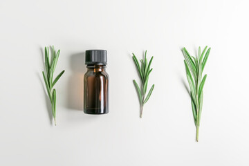 rosemary essential oil in a yellow glass bottle and rosemary sprigs on a white background, top view