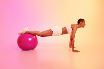 A disciplined woman with a shaved head holds a plank position on a pink exercise ball
