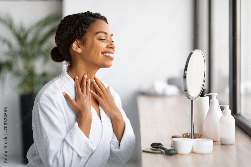 Wall mural Beauty Care. Beautiful Black Female Touching Neck Skin And Looking In Mirror