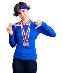 Beautiful young woman with short hair wearing winner medals with angry face, negative sign showing dislike with thumbs down, rejection concept