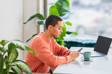 A young woman in a vibrant orange sweater is engrossed in her smartphone