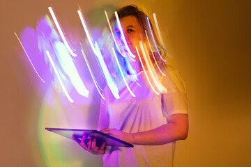 Girl wired for success with digital tablet in vibrant neon multicolored light. Bold workspace with beautiful girl in white shirt working