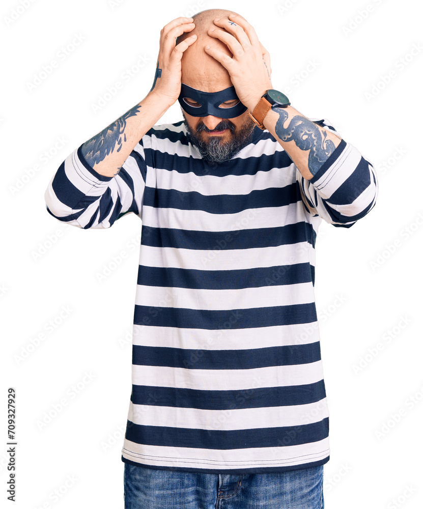 Wall mural Young handsome man wearing burglar mask suffering from headache desperate and stressed because pain and migraine. hands on head.