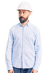 Young handsome man wearing architect hardhat smiling looking to the side and staring away thinking.